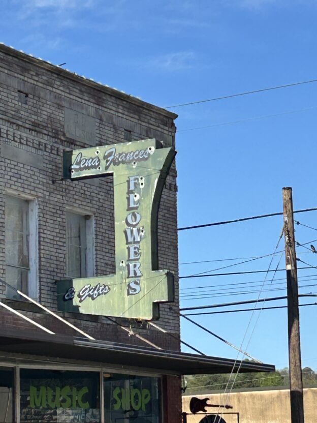 A downtown Harrison building with a faded painted wall sign and an old Lena Frances Flowers & Gifts projecting sign above the sidewalk.